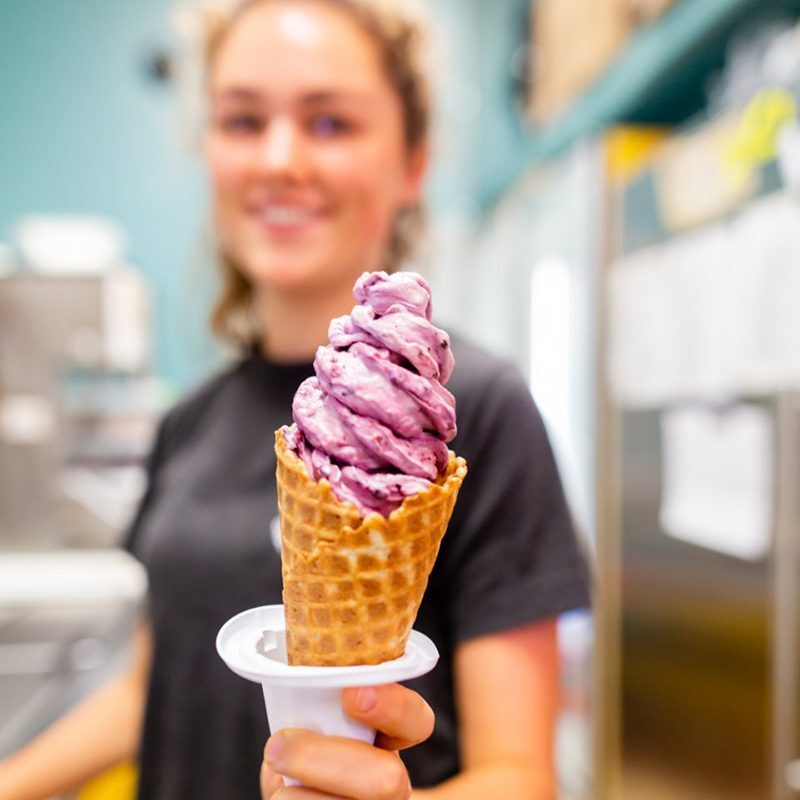 A woman holding up an ice cream cone in front of her.